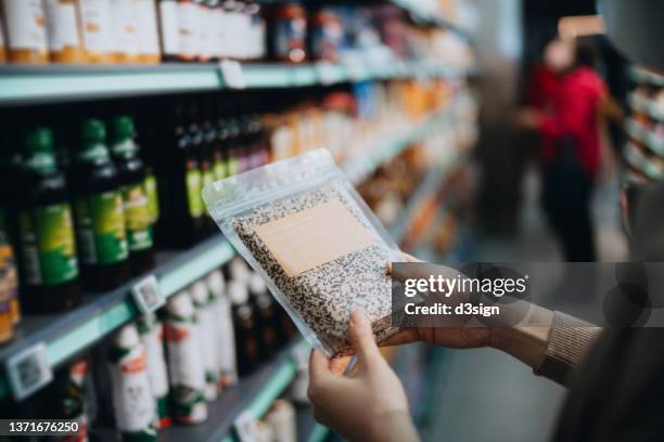 cropped shot of young asian woman grocery shopping for healthy food in a supermarket, holding a packet of organic tricolour quinoa and examining the nutrition values on the label. healthy eating lifestyle. making healthier food choices - bio supermarkt stockfoto's en -beelden