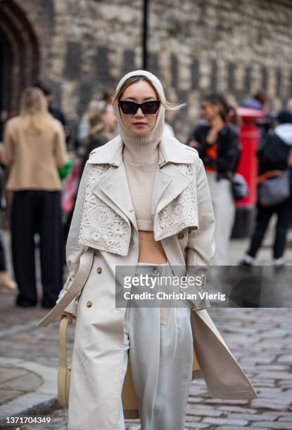 Betty Bachz seen wearing cropped jumper with balaklava, trench coat, creme white pants, beige bag, sunglasses outside Eudon Choi during London...