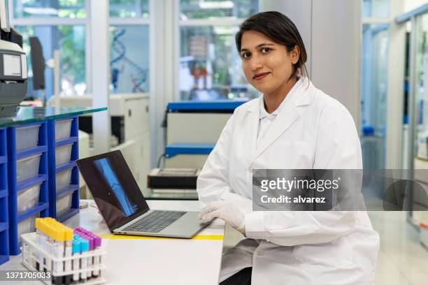 portrait d’une femme scientifique assise à son bureau avec un ordinateur portable - pathologist photos et images de collection