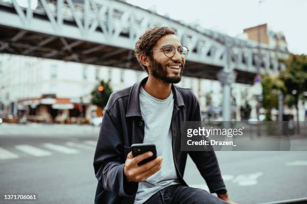 modern young man with curly hair in the city using smart phone, copy space on the image. - sassy paris stock pictures, royalty-free photos & images