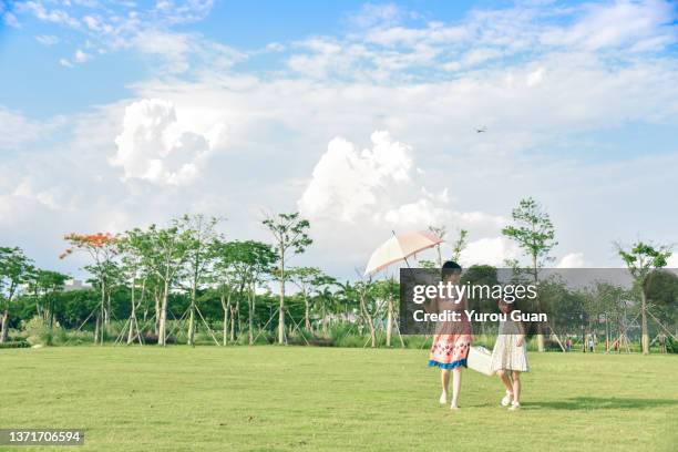 an elegant asian female mother ( 25-29 years ) and her daughter （ 6-7 years ) walks on the park lawn with a laundry basket, jiangmen, guangdong, china. - years of italian style launch party outside arrivals stockfoto's en -beelden