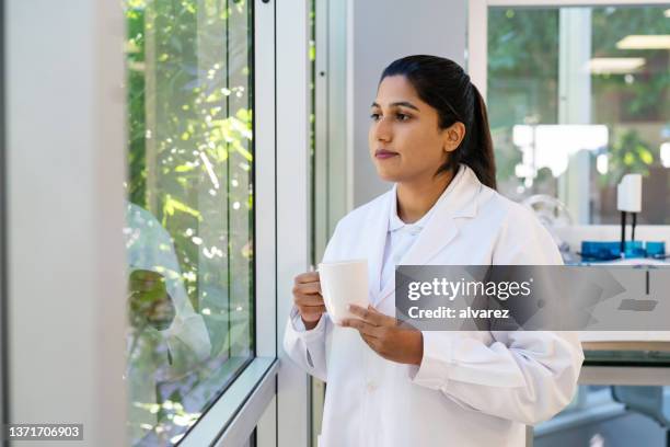 scientifique avec un café regardant à l’extérieur de la fenêtre du laboratoire - biochimiste photos et images de collection