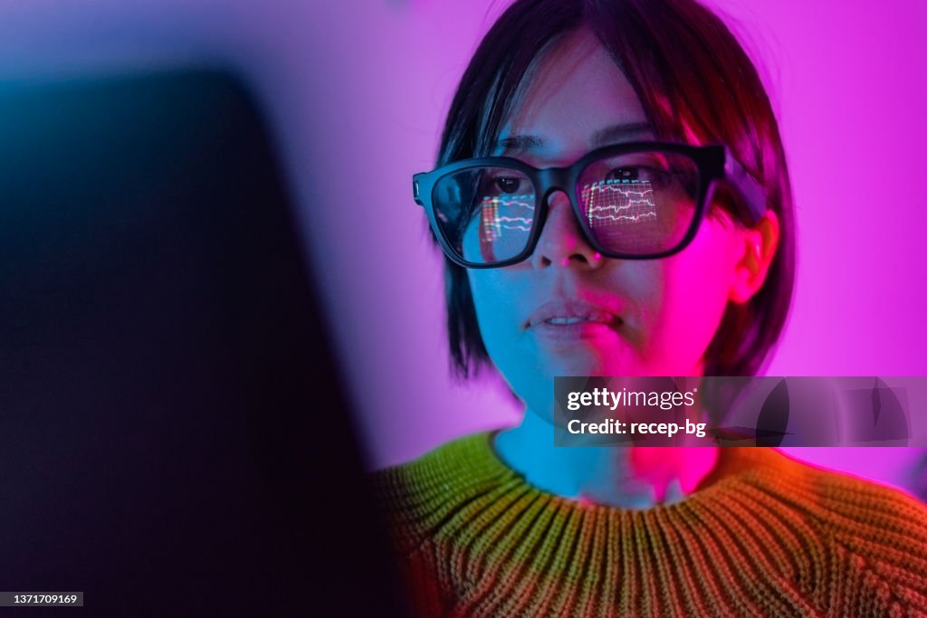 Woman checking chart for currency information on laptop. Cryptocurrency chart reflected on smart glasses.