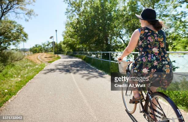 young woman riding her bike along a park path in summer - calgary summer stock pictures, royalty-free photos & images