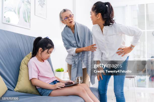 angry mother scolding the disobedient child playing tablet at home - asian violence stock pictures, royalty-free photos & images
