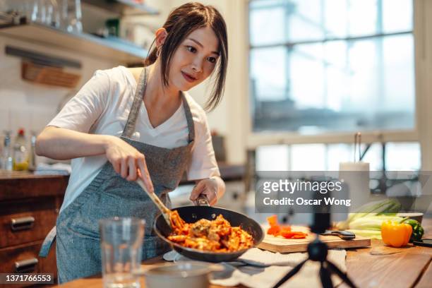 female food blogger cooking pasta and recording video on smart phone - side hustle stock pictures, royalty-free photos & images