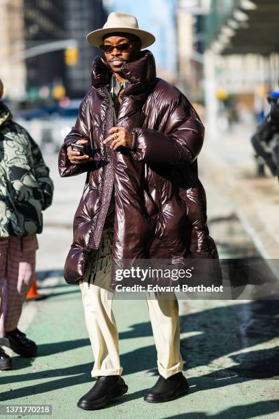 Guest wears a beige felt / wool hat, sunglasses, a black with multicolored print pattern shirt, a beige and black print pattern blazer jacket, a...