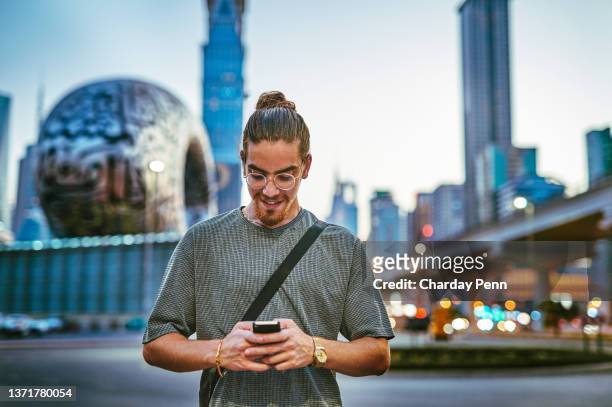 shot of a handsome young man standing alone in the city and using his cellphone during the evening - map of the uae stock pictures, royalty-free photos & images