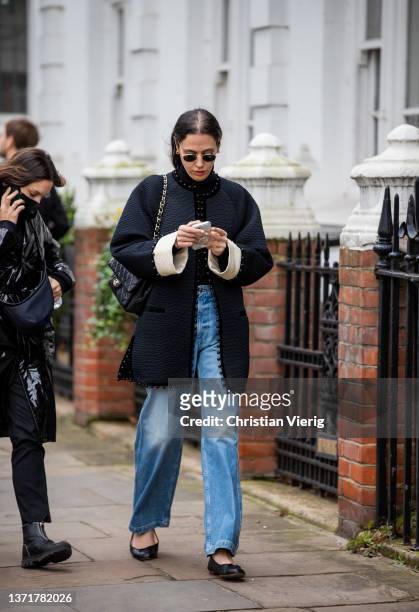 Guest is seen wearing denim jeans, black jacket with beige sleeve, black Chanel bag, flat shoes outside Eudon Choi during London Fashion Week...