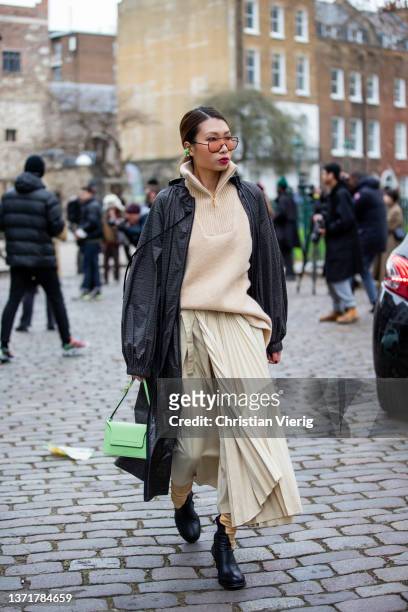 Guest is seen wearing beige jumper with zipper, pleated skirt, grey coat, green bag outside Eudon Choi during London Fashion Week February 2022 on...