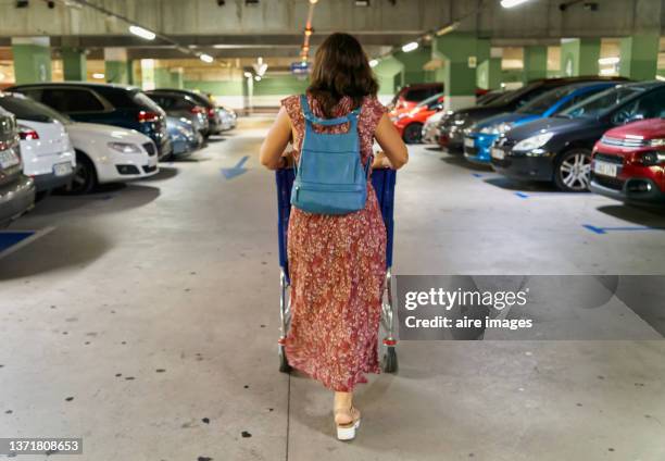 woman walking in shopping mall parking lot, pushing shopping carts, different models of parked cars. ready to go home. - estacionamento de carros imagens e fotografias de stock