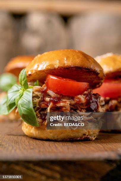 Close up of homemade mini burgers with stew beef, tomatoes and basil on wooden background, Modern delicious fast food, Low angle view.