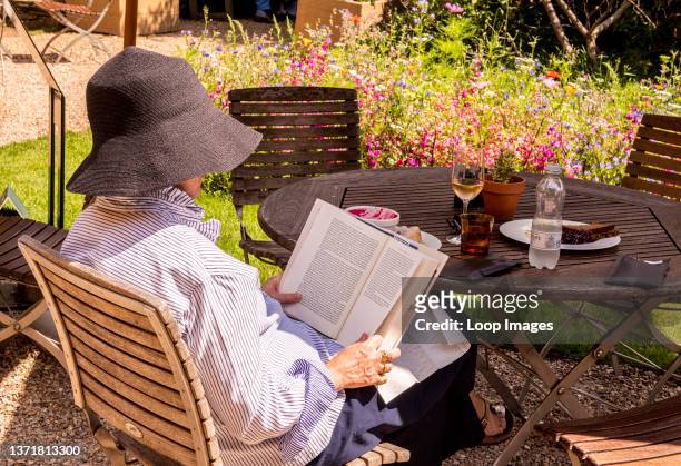 Woman wearing a big sun hat is reading peacefully in the cafe of the Chelsea Physic Garden in Central London.