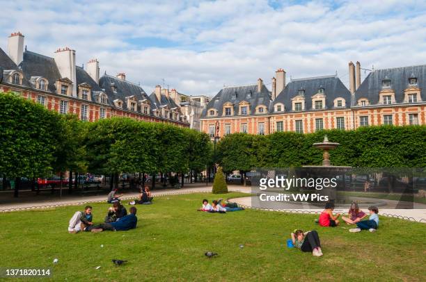 People relaxing on the grounds of Place des Vosges. Place des Vosges, Paris, Ile-de-France. France..