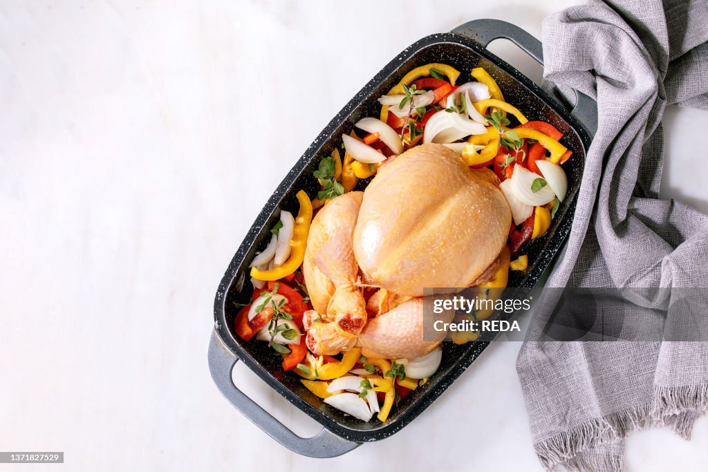 Raw organic uncooked whole chicken with sliced vegetables bell pepper. onion and herbs in oven tray with grey textile napkin. ready to cook. White marble backgrouns. Top view. flat lay. Copy space