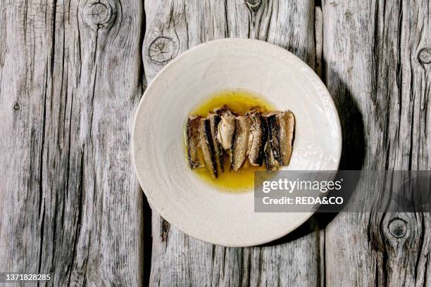 Smoked sardines in oil served in white ceramic plate over old grey wooden background. Top view. Flat lay. Copy space.