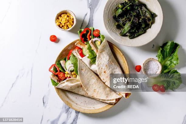 Homemade traditional mexican tortila wrap with pork meat and vegetables in ceramic plate served with grilled green peppers jalapenos. Corn and salt...