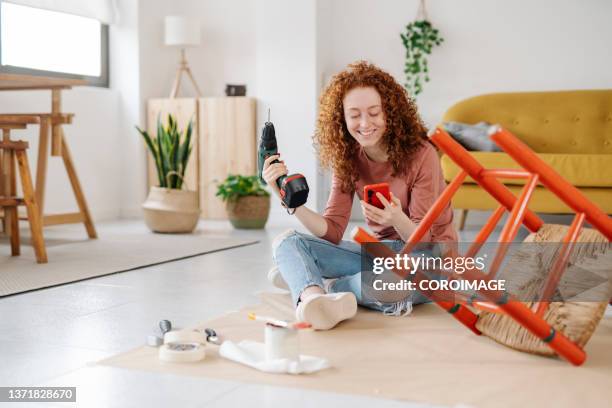woman using a mobile phone while renovating and repairing an old chair. - handy fotografías e imágenes de stock