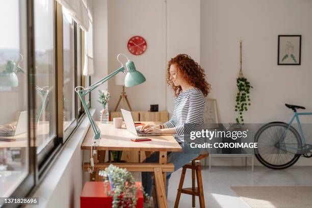 woman sitting on a desk using a laptop computer while working from home. - the independent stockfoto's en -beelden