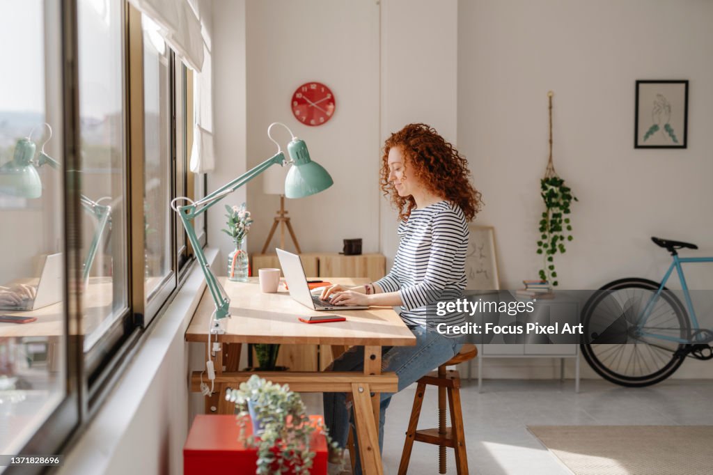 Woman sitting on a desk using a laptop computer while working from home.