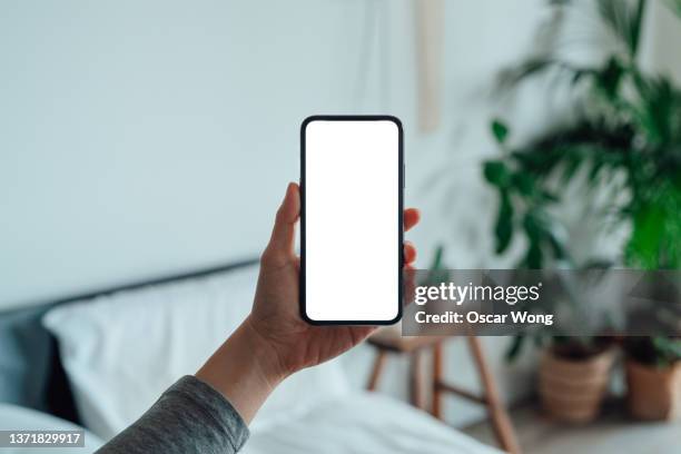 female hand holding smartphone with blank screen in the bedroom - holding imagens e fotografias de stock