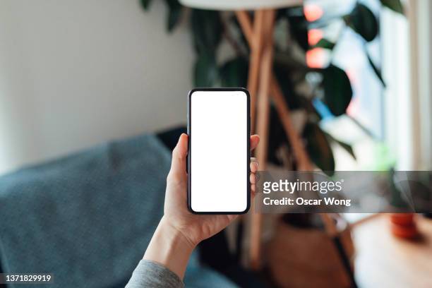female hand holding smartphone with blank screen in the living room - smart phone foto e immagini stock