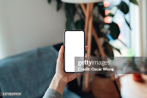 Female hand holding smartphone with blank screen in the living room Female hand holding smartphone with blank screen in the living room