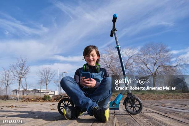 teenager sitting next to his scooter using a smart phone - elektro tretroller stock-fotos und bilder