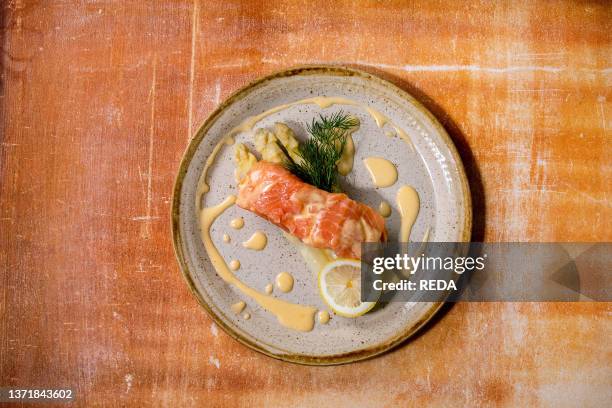 Cooked salmon fish on homemade ceramic plate served with white asparagus. Lemon. Dill and hollandaise sauce over orange stone texture backgrpund. Top...