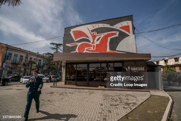 Military officer checks his phone as he marches briskly past a prominent mosaic near the seafront in Sukhum in Abkhazia.