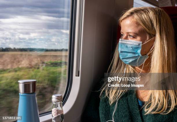 Woman wearing face mask on train looking through window.