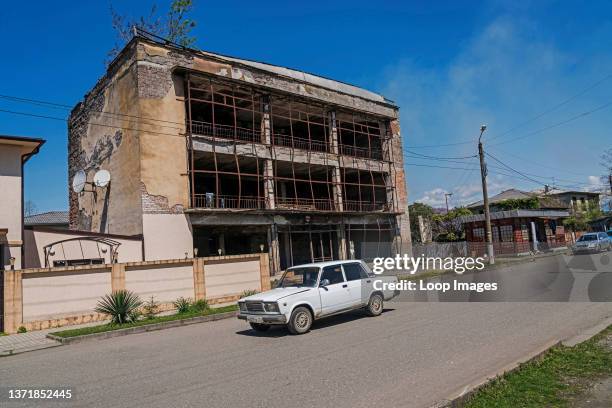 Soviet era car rolls past a ruined building in Ochamchire in Abkhazia.