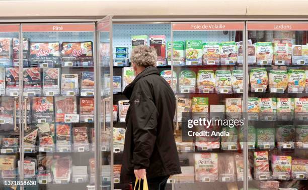 A man in the middle of the fresh food department, vacuum packed cooked cold meat, protege, poultry liver, diced bacon.