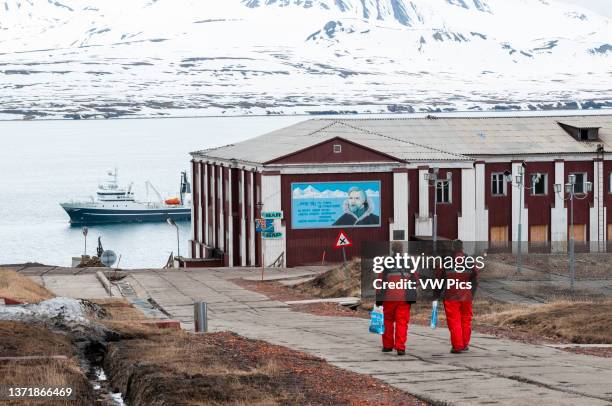 Men in arctic protective clothing walk toward an anchored ship. Barentsburg, Spitsbergen Island, Svalbard, Norway..