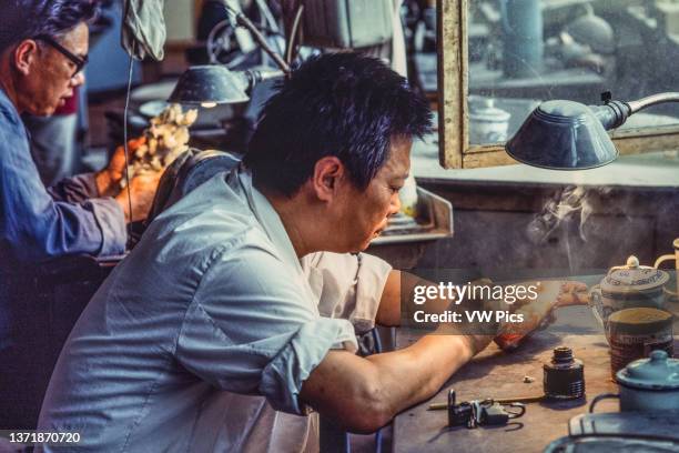 An artisan in a jade factory works on a jade figurine whlie smoking a cigarette. Beijing, China..