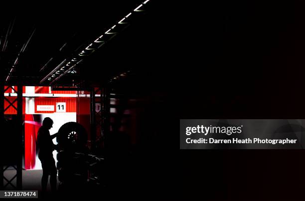 Photographed in silhouette, a Scuderia Ferrari Formula One racing team mechanic working outside the rear entrance to the team's pit lane, pit garage...