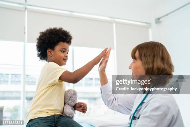 caucasian doctor and boy high-fiving in doctor office - ethnicity fotografías e imágenes de stock