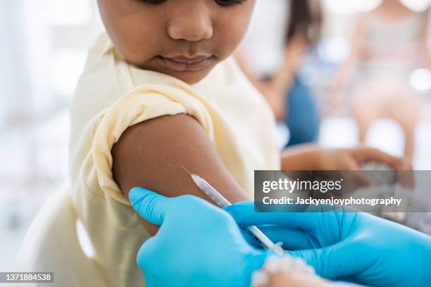 immunisation. protecting children from diseases. close-up nurse in medical gloves giving injection to little patient. brave boy getting a flu shot at doctor's office and looking at needle - vacina imagens e fotografias de stock