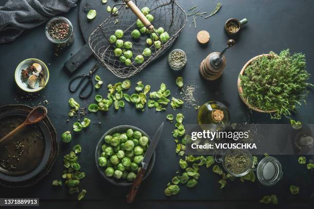 brussel sprouts at dark kitchen table with wooden spoon, bowls, herbs, metal basket, oil, pepper mill and spices - pepper mill - fotografias e filmes do acervo