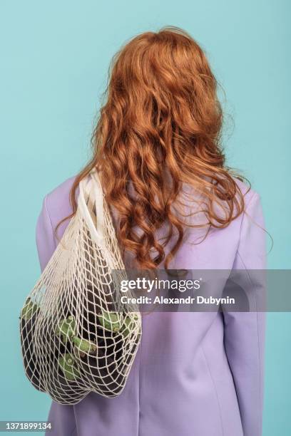 back view woman holding a string bag with eggplant on a colored background - bio supermarkt stock-fotos und bilder