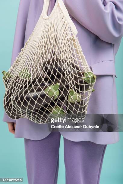 a woman's hand holds a string bag with eggplant on a colored background - reusable bag isolated stock pictures, royalty-free photos & images