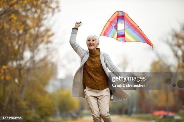 cheerful senior woman running with a kite in the park. - kite toy stock pictures, royalty-free photos & images