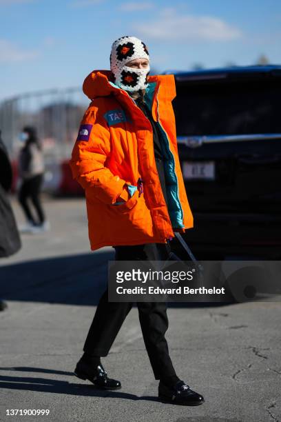 Guest wears a white with black and orange print pattern balaclava, a neon orange with green and purple embroidered yoke puffer jacket from The North...