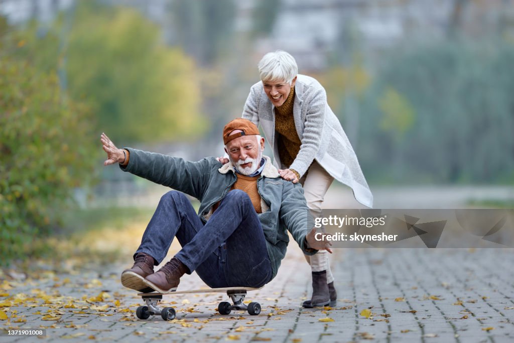 Playful senior couple having fun on skateboard in the park.