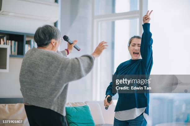 asian chinese senior woman singing karaoke dancing with her daughter in living room during weekend leisure activities - chinese mothers day stockfoto's en -beelden
