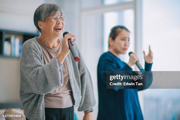 asian chinese senior woman singing karaoke dancing with her daughter in living room during weekend leisure activities - karaoke stock pictures, royalty-free photos & images