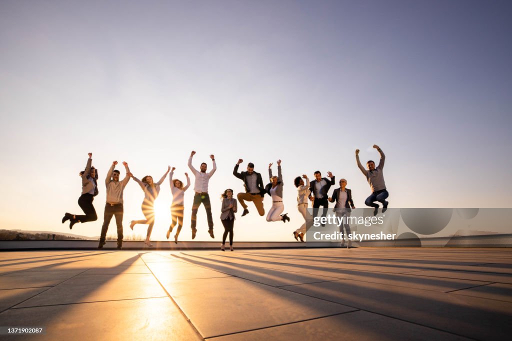 Playful entrepreneurs jumping on a rooftop at sunset.