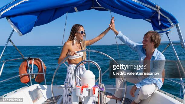 close up  of a young couple relaxing on a sailboat cruise while sailing. they are having some wine, chatting and laughing, while the girl is navigating the sailboat. - boat steering wheel stock pictures, royalty-free photos & images