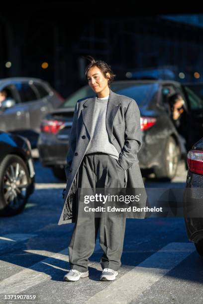 Guest wears a white t-shirt, a pale gray wool pullover, a gray oversized jacket coat, gray suit pants, a black shiny leather handbag, pale gray suede...