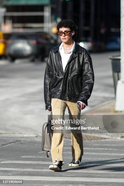 Guest wears black sunglasses, a white shirt, a black shiny leather oversized jacket, a beige suede flared pants, a gray shiny leather large pants,...